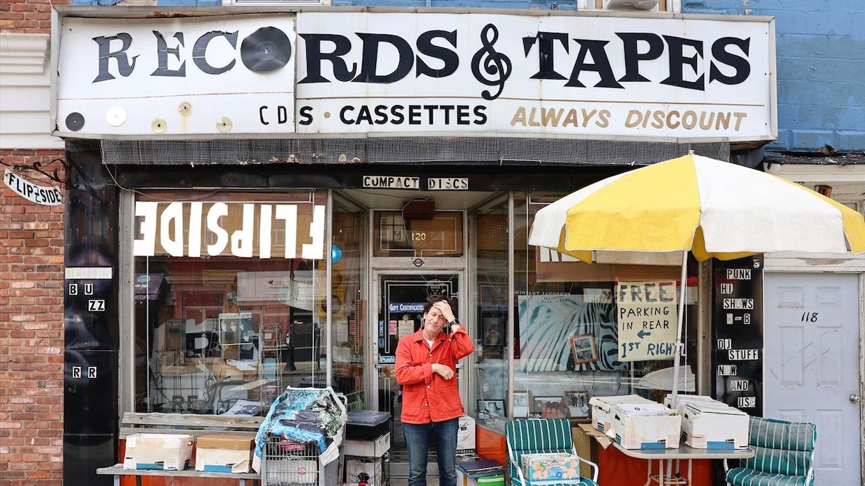 A man clutches his forehead standing beneath the awning of a record store.