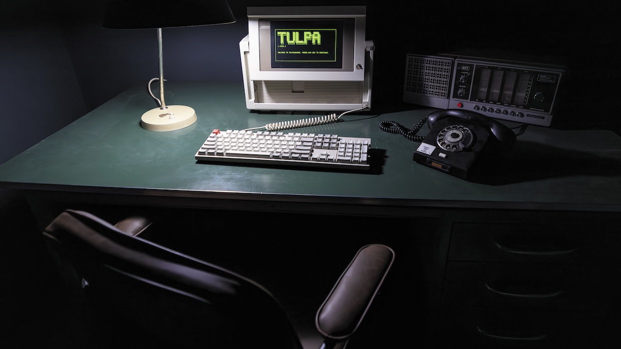An old desktop computer with the word "Tulpa" on the monitor rests on a green table.