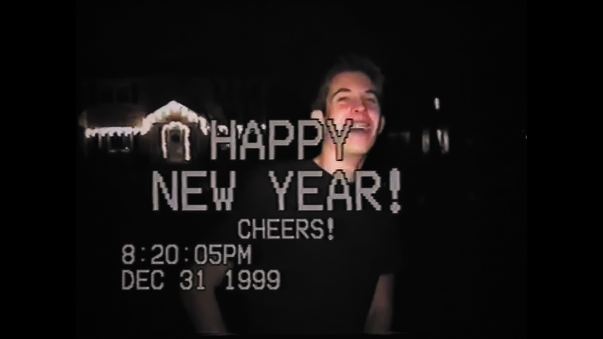 A man smiles in VHS camcorder footage from New Year's Eve, 1999.