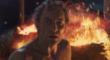 A painted image of a shirtless middle-aged man standing in front of a blazing fire outdoors.