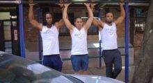 Three men in workout clothes are grasping a pull-up bar.