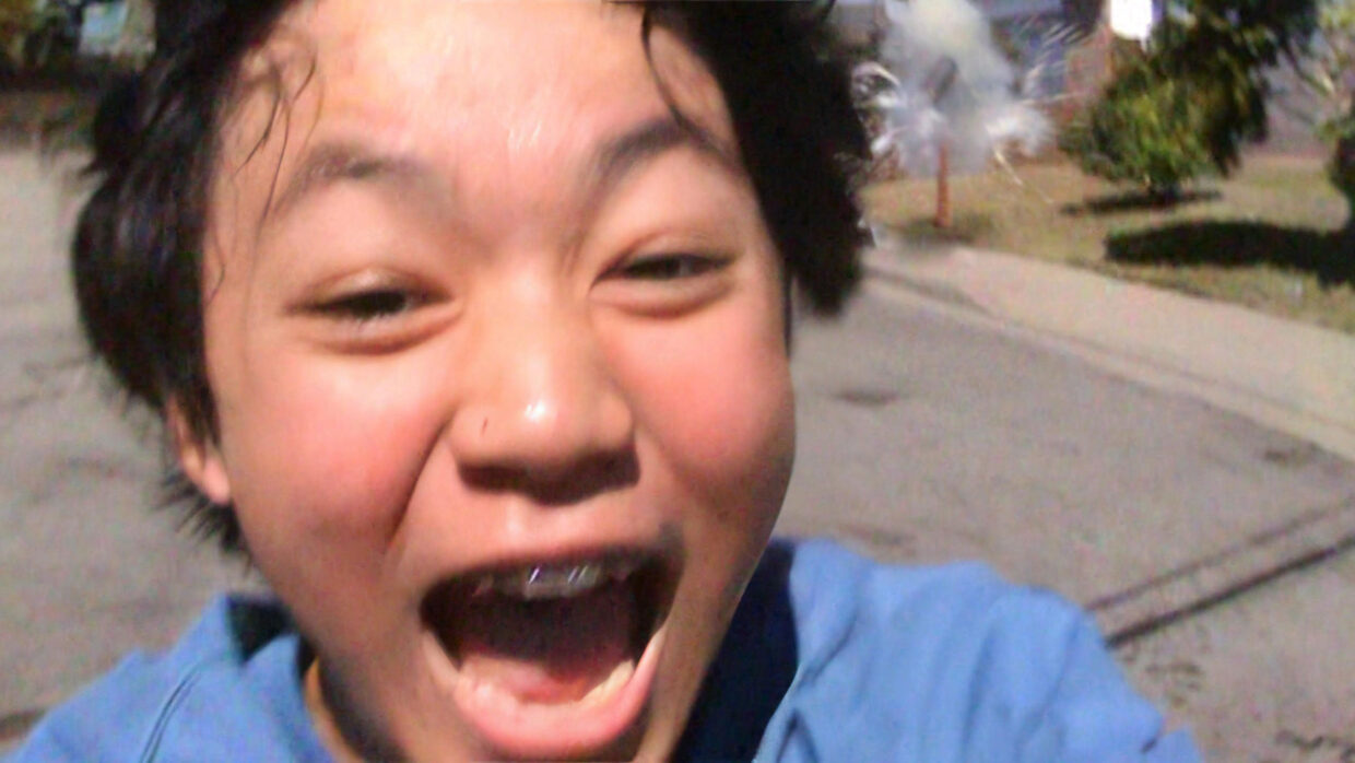 A young adolescent Asian boy is joyously yelling in close-up.