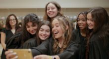A diverse group of high school girls take a group selfie.