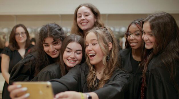 A diverse group of high school girls take a group selfie.