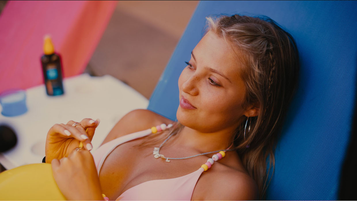 A young woman in a peach bikini top lounges on a blue beach chair, her hair wet from recently swimming.