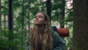 A white teenage girl with a camping backpack looks up in the forested Pacific Northwest.