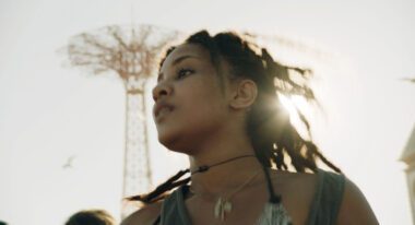 A young Black woman stands in front of a Coney Island ride.