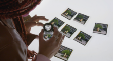An African-American woman is looking through a magnifying glass at photographs laid out on a table.