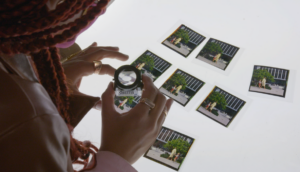 An African-American woman is looking through a magnifying glass at photographs laid out on a table.