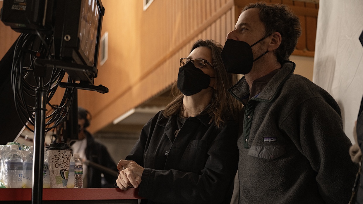 A woman and man, both wearing face masks, watch a monitor on-set.