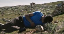 A man in a blue t-shirt lies on a rocky landscape.