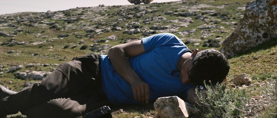 A man in a blue t-shirt lies on a rocky landscape.