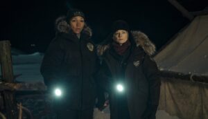 Two women shine their flashlights while standing in a dark, snowy landscape.