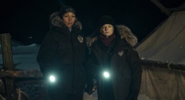 Two women shine their flashlights while standing in a dark, snowy landscape.