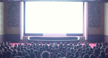 A white movie screen pours light onto a full auditorium of moviegoers.