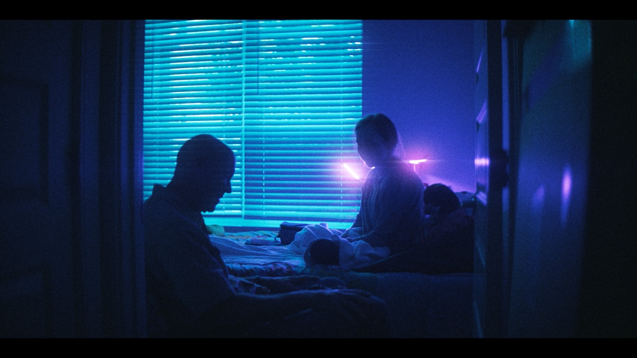 Two people, visible in silhouette, sit in a blue-and-purple-lit room.