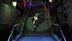 A woman in a green wig and tights dances down a stairwell.