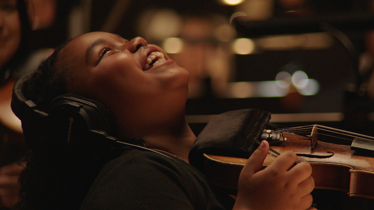 A young child smiles while playing the violin.