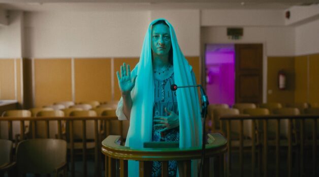 A woman bathed in turquoise light raises her hand to testify in a courtroom.