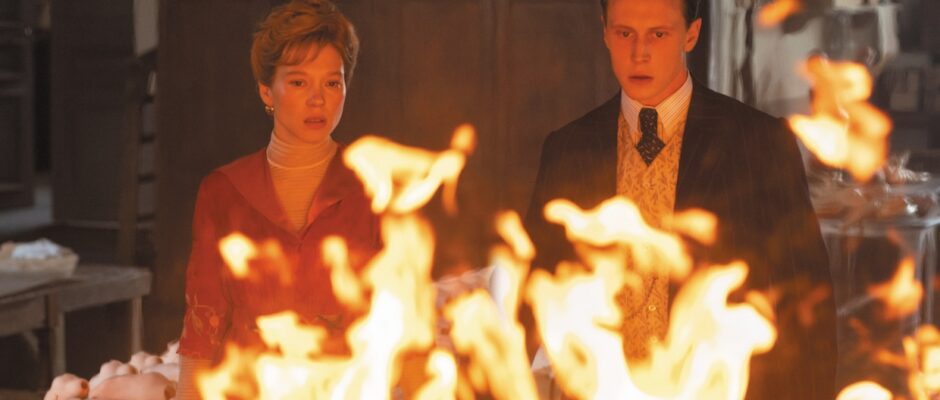 A woman and man stare at a fire in a doll factory.