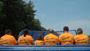 A row of people with their backs to the camera sit on a boat wearing orange t-shirts.