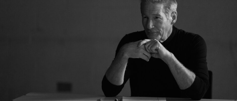 A white man sits behind a desk.