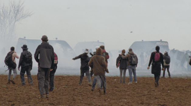 Protesters walk over a field through clouds of tear gas.
