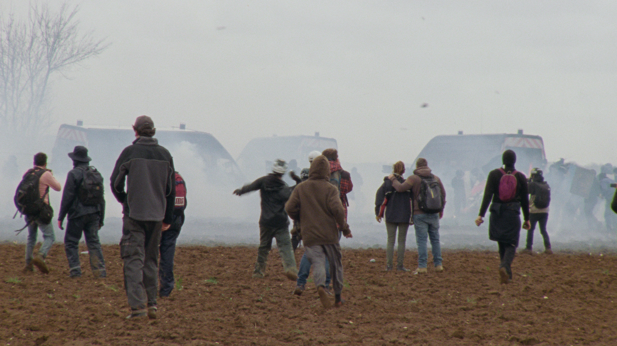 Protesters walk over a field through clouds of tear gas.