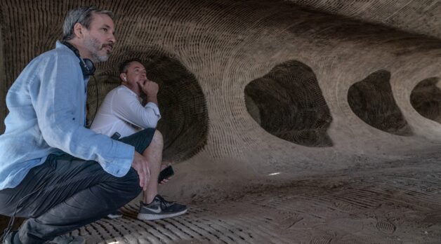 Two white men crouch in a cave.
