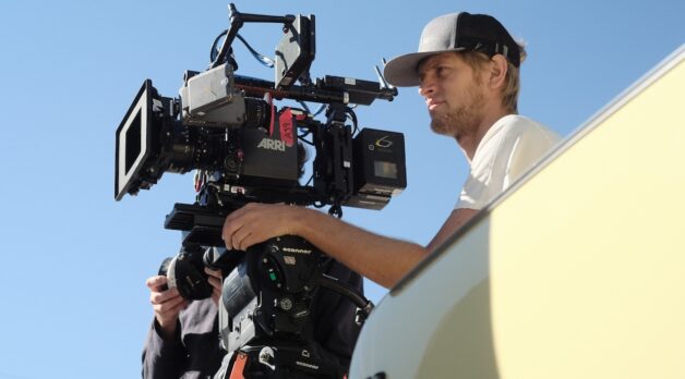 A cinematographer stands behind a camera on an outdoor set.