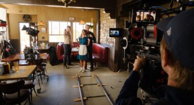 On a diner film set, two men direct an actress dressed as a waitress.