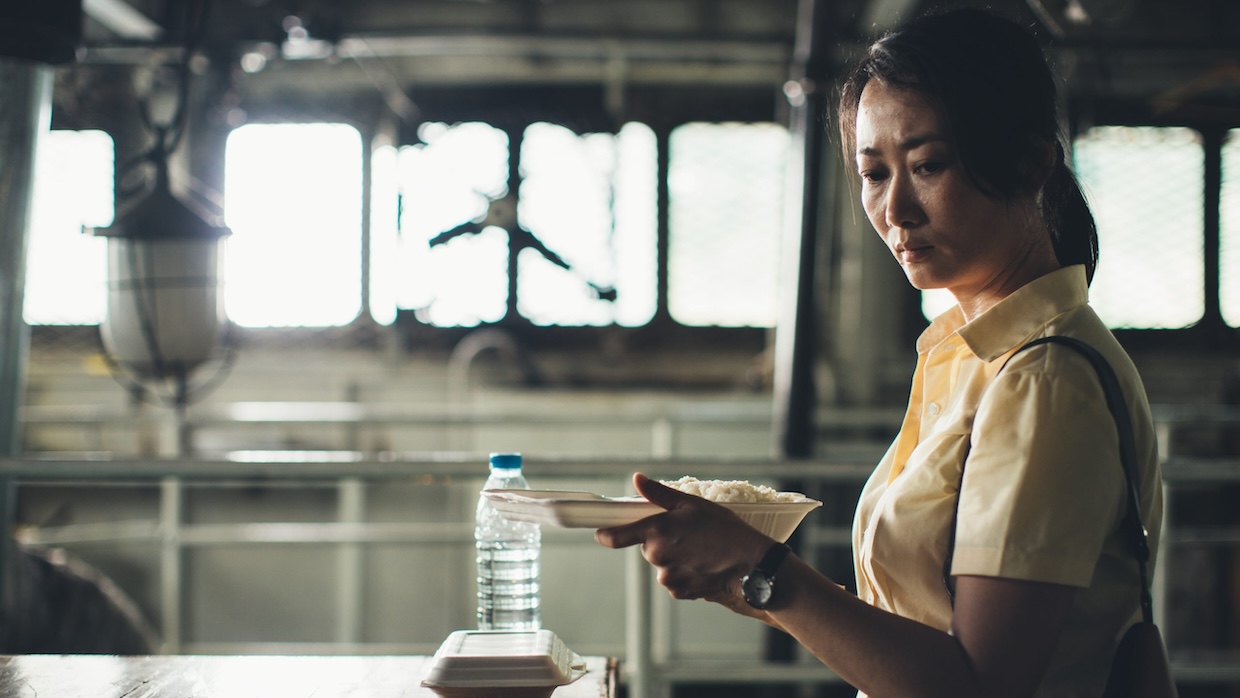 A Chinese woman holds a styrofoam container of rice while eating on a deserted boat deck.