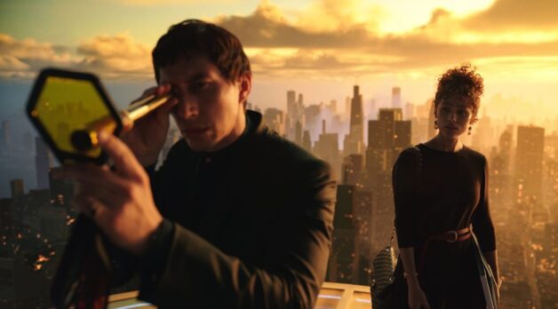 A man looks over a city landscape through a telescope at sunset while a woman stands behind him.