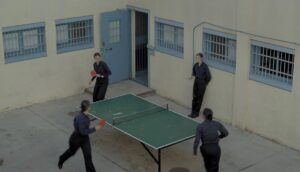 Three people play ping-pong while one watches in a courtyard.