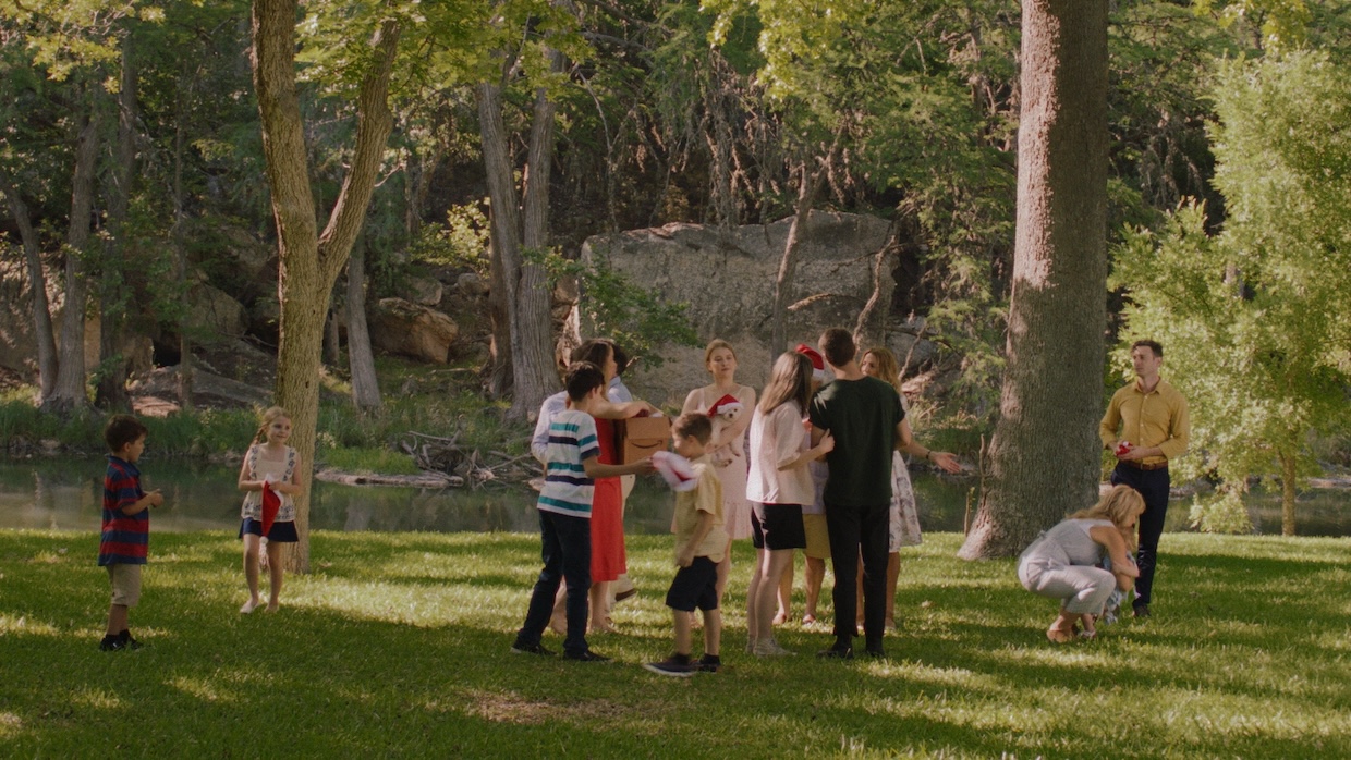 A large extended family of white people mills around a sunny, park-like landscape.