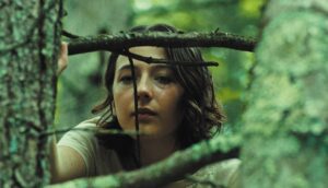 A young white teenager gazes out through tree branches in a forest.