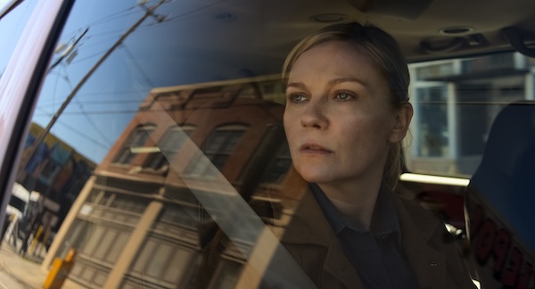 A white woman stares out of a moving car's window at the building of a town.