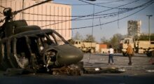 Two women walk past a helicopter that's crashed din a parking lot.
