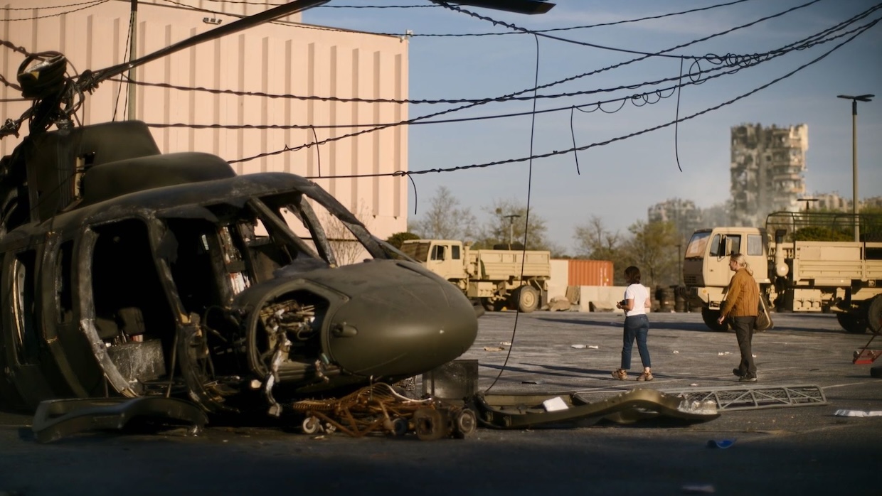 Two women walk past a helicopter that's crashed din a parking lot.