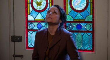 A white woman stares up against a wall of stained glass.