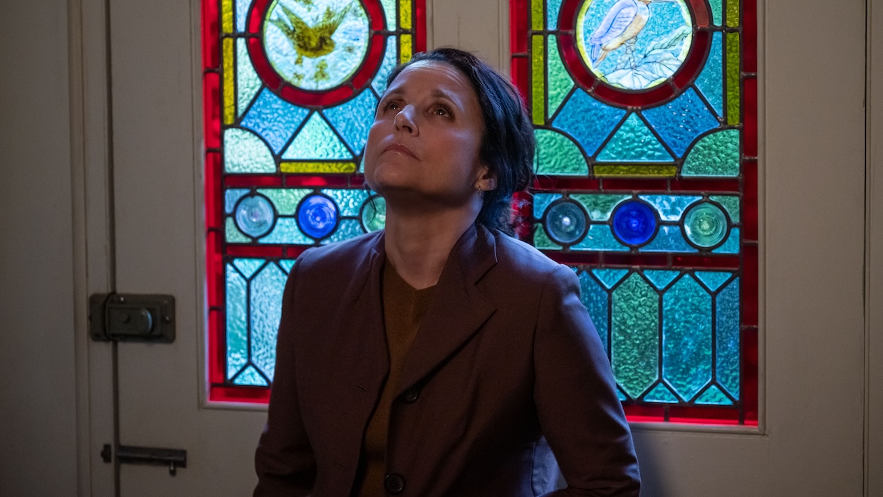 A white woman stares up against a wall of stained glass.