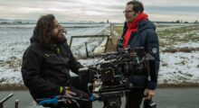 A cinematographer and film director stand around a film camera on a set.