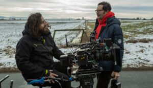 A cinematographer and film director stand around a film camera on a set.