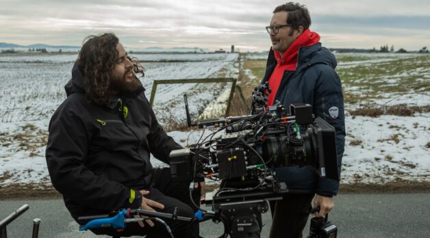 A cinematographer and film director stand around a film camera on a set.