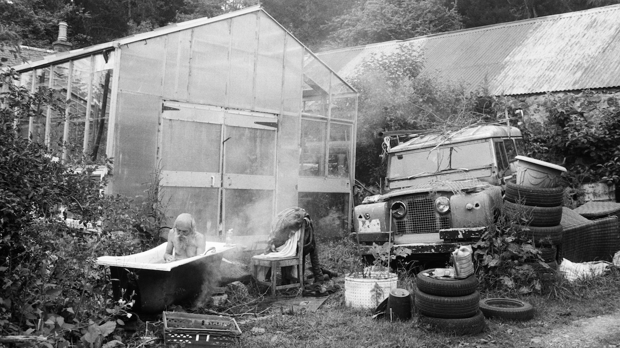 A man with a large beard takes a bath outside in a steaming tub.