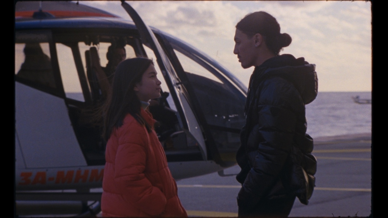 A teenage girl and an older teenage boy stand on a helicopter pad.