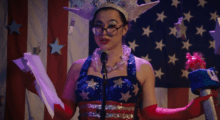 A woman in glasses recites onstage while clad in an American flag top.