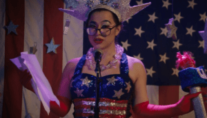 A woman in glasses recites onstage while clad in an American flag top.