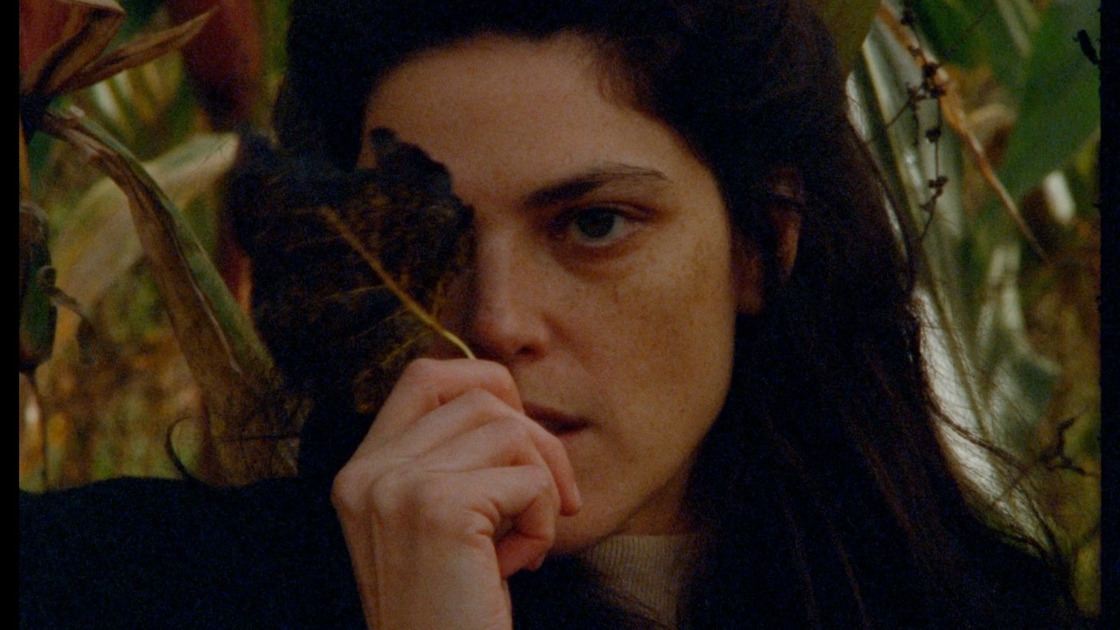 A young woman holds a black leaf in front of her right eye.