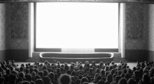 An audience sits before a large blank screen in a movie theater.